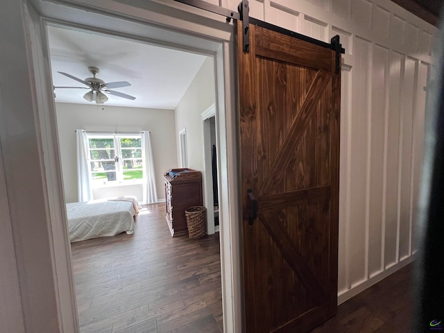 bedroom with dark hardwood / wood-style floors, ceiling fan, and a barn door