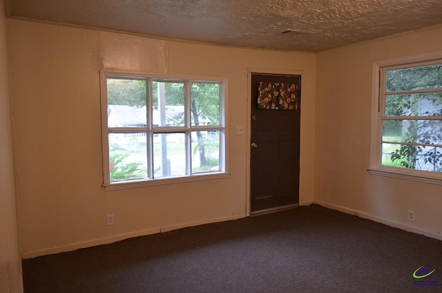 spare room featuring a textured ceiling, dark carpet, and baseboards