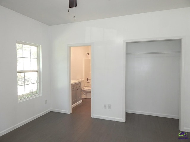 unfurnished bedroom with a closet, dark wood-style flooring, ensuite bath, and baseboards