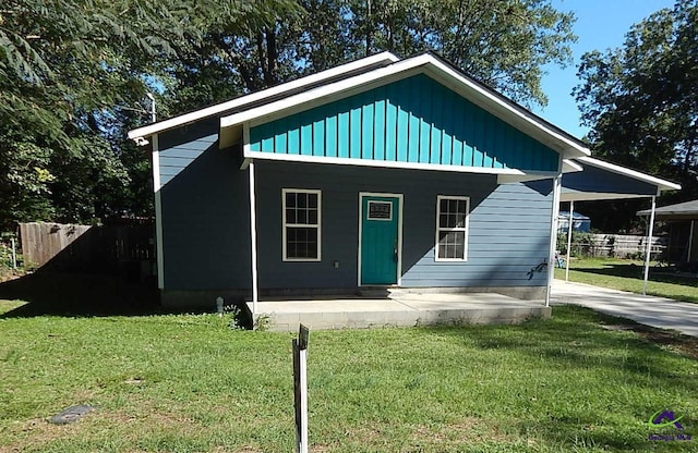 view of front of property featuring covered porch, fence, a carport, a front lawn, and board and batten siding