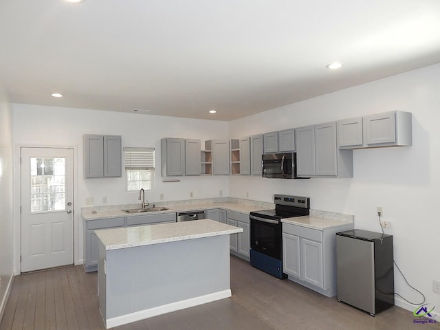 kitchen with wood finished floors, stainless steel appliances, gray cabinetry, open shelves, and a sink