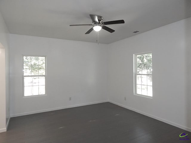 spare room with ceiling fan, visible vents, baseboards, and dark wood-type flooring