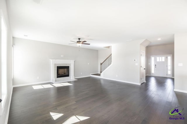 unfurnished living room featuring ceiling fan, baseboards, stairs, a premium fireplace, and dark wood-style floors