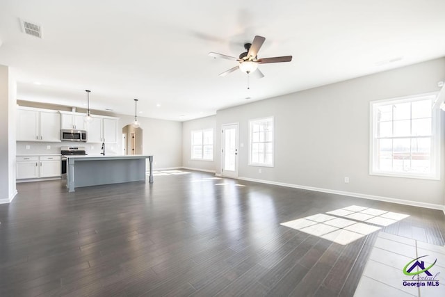 unfurnished living room with ceiling fan, visible vents, baseboards, and dark wood finished floors