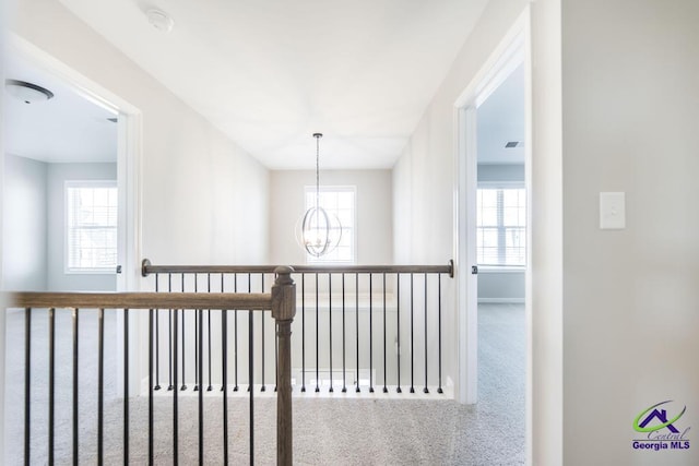 hallway featuring visible vents, a healthy amount of sunlight, an inviting chandelier, and carpet