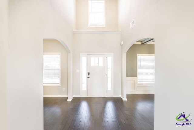 foyer entrance with visible vents, wainscoting, a towering ceiling, and dark wood-style flooring