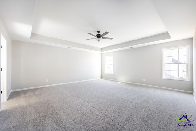 carpeted spare room featuring ceiling fan, a raised ceiling, and baseboards