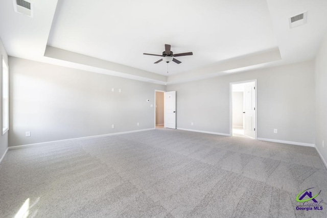 unfurnished room featuring a tray ceiling, carpet, and visible vents