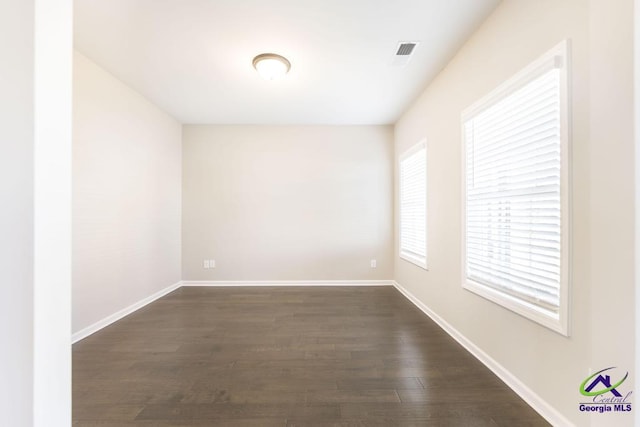 unfurnished room featuring dark wood-style floors, visible vents, and baseboards