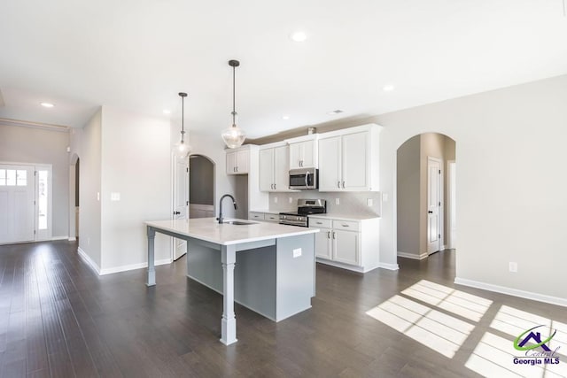 kitchen featuring a sink, stainless steel appliances, arched walkways, and a kitchen island with sink