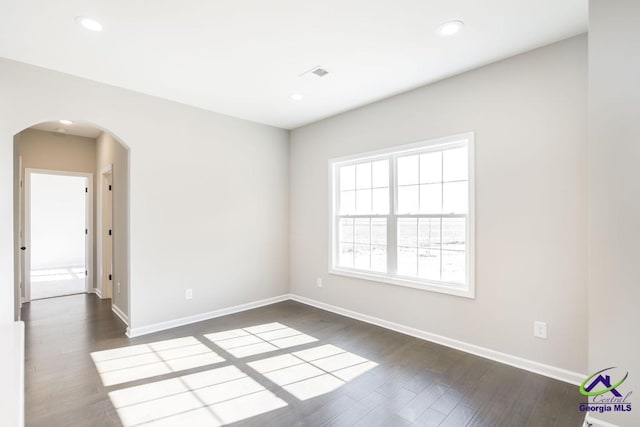 empty room featuring recessed lighting, baseboards, arched walkways, and dark wood-style flooring