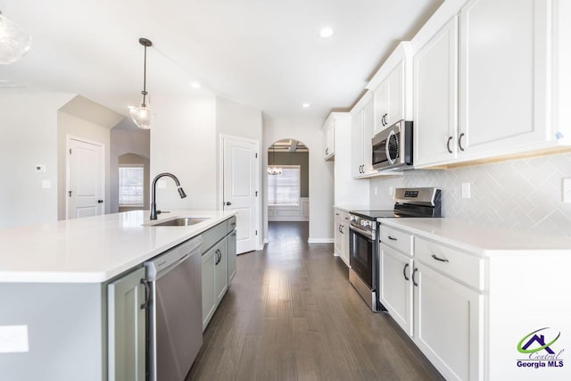 kitchen featuring decorative light fixtures, an island with sink, sink, white cabinets, and stainless steel appliances