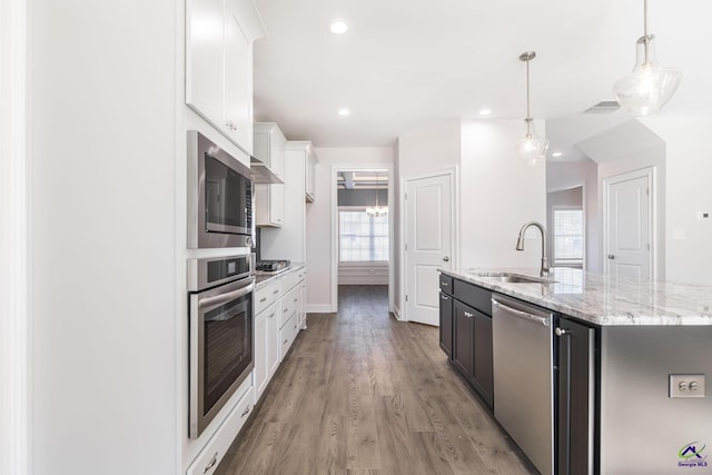 kitchen featuring white cabinets, stainless steel appliances, an island with sink, sink, and hanging light fixtures