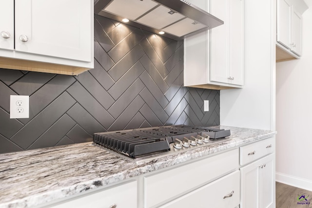 kitchen with backsplash, white cabinetry, hardwood / wood-style flooring, light stone countertops, and wall chimney exhaust hood