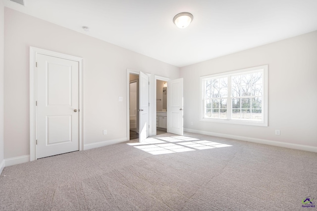 unfurnished bedroom with light colored carpet and connected bathroom