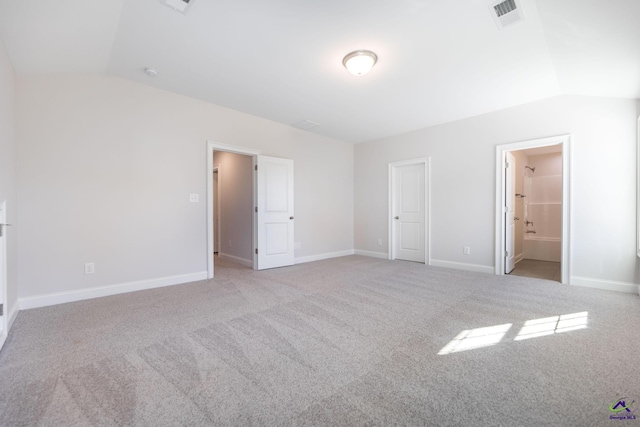 unfurnished bedroom with light carpet, ensuite bathroom, and lofted ceiling