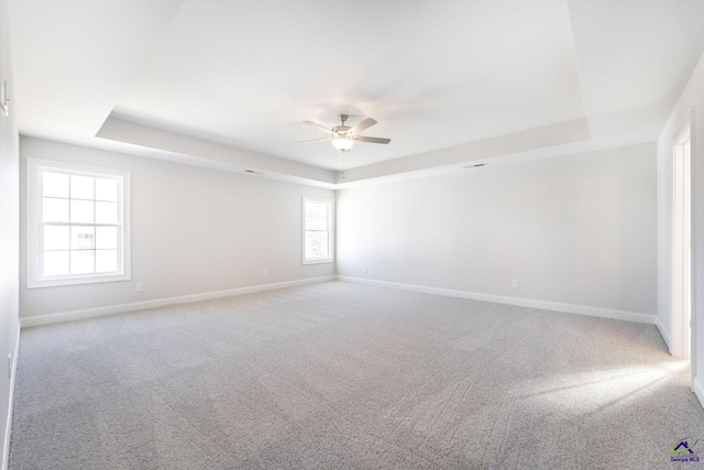 empty room featuring ceiling fan, light colored carpet, and a tray ceiling