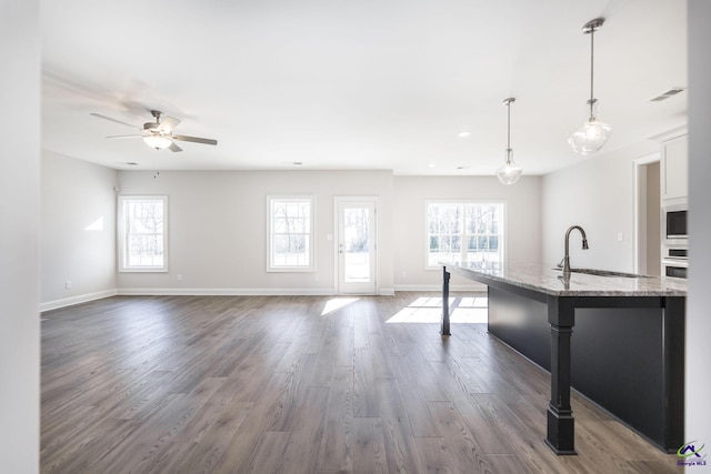 kitchen with a center island with sink, a kitchen breakfast bar, white cabinets, hanging light fixtures, and light stone counters