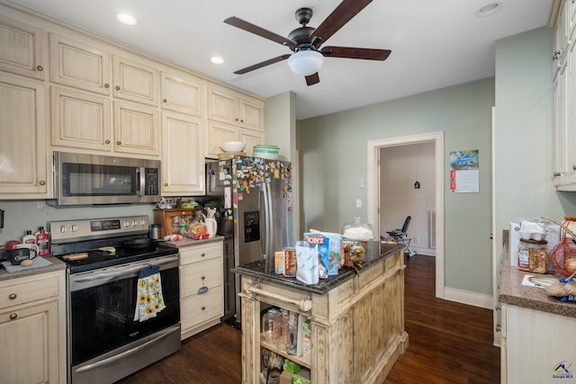 kitchen featuring appliances with stainless steel finishes, dark hardwood / wood-style flooring, dark stone counters, cream cabinetry, and ceiling fan