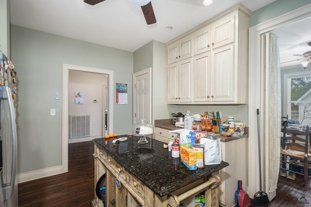 kitchen featuring dark hardwood / wood-style floors, stainless steel fridge, dark stone countertops, cream cabinetry, and ceiling fan