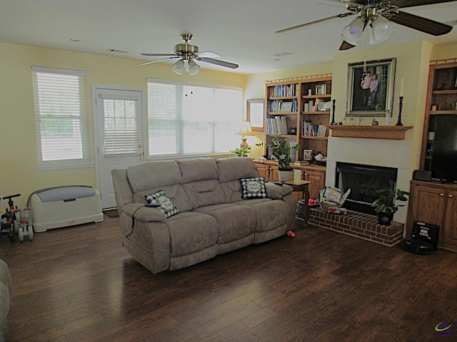 living room with dark wood-type flooring, ceiling fan, and a brick fireplace