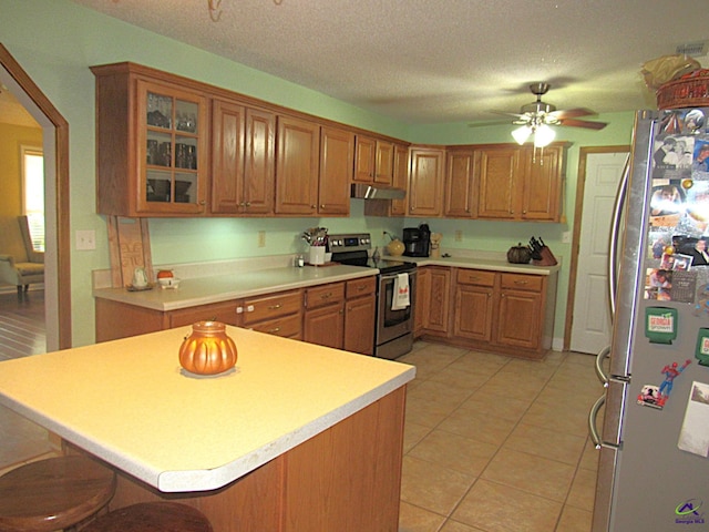 kitchen featuring ceiling fan, a textured ceiling, stainless steel appliances, and a breakfast bar area