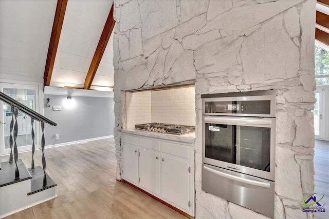 kitchen featuring vaulted ceiling with beams, appliances with stainless steel finishes, light wood-type flooring, and white cabinets