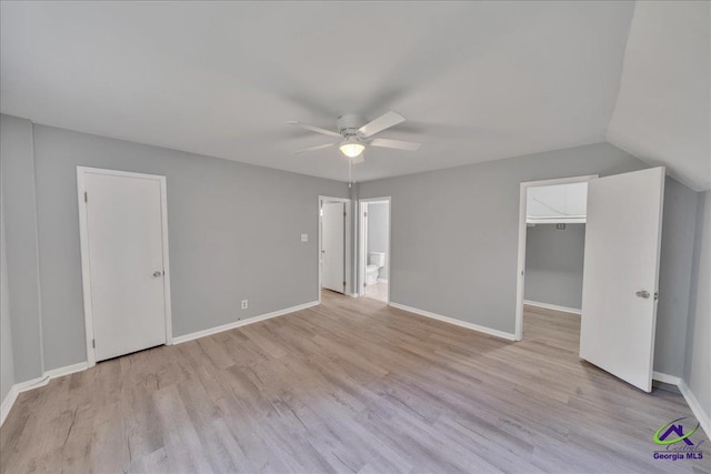 unfurnished bedroom with a closet, a walk in closet, vaulted ceiling, light wood-type flooring, and ceiling fan