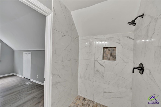 bathroom featuring a tile shower, lofted ceiling, and wood-type flooring