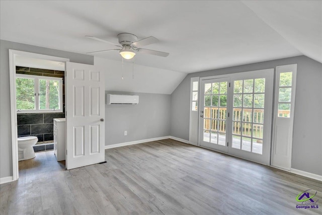 additional living space featuring a wealth of natural light, vaulted ceiling, a wall mounted air conditioner, and light wood-type flooring