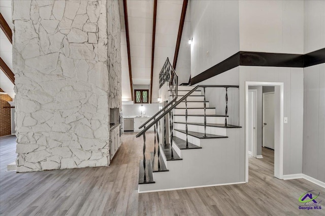 staircase with beamed ceiling, hardwood / wood-style floors, and a towering ceiling