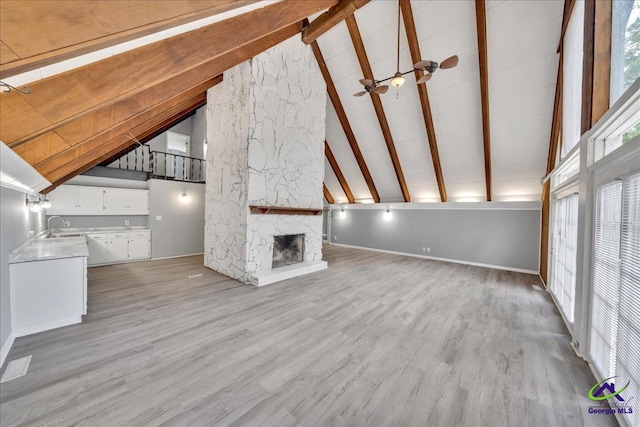 unfurnished living room with a stone fireplace, high vaulted ceiling, light wood-type flooring, and ceiling fan