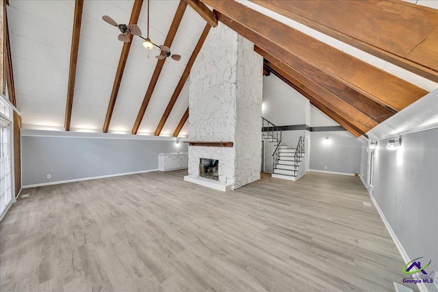 unfurnished living room with light hardwood / wood-style floors, beam ceiling, a stone fireplace, and high vaulted ceiling