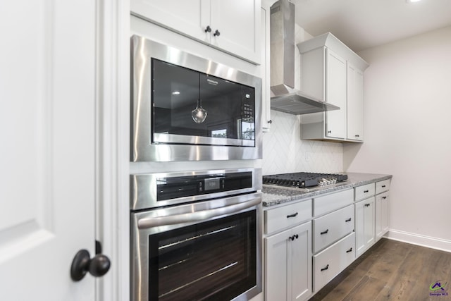 kitchen featuring appliances with stainless steel finishes, white cabinetry, wall chimney range hood, dark hardwood / wood-style flooring, and stone counters