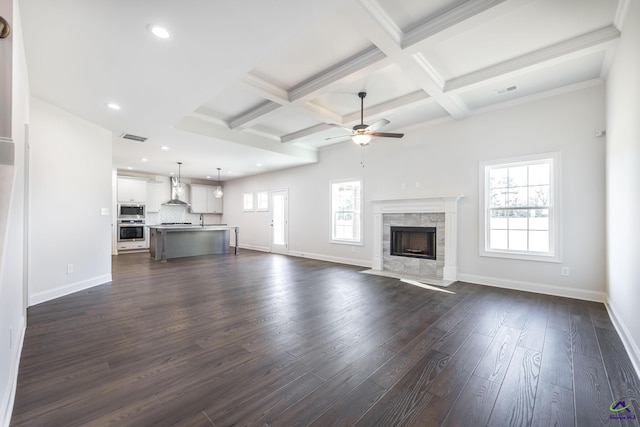 unfurnished living room featuring a high end fireplace, dark wood-type flooring, ceiling fan, beam ceiling, and coffered ceiling