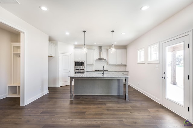 kitchen with white cabinetry, wall chimney range hood, appliances with stainless steel finishes, and a kitchen island with sink