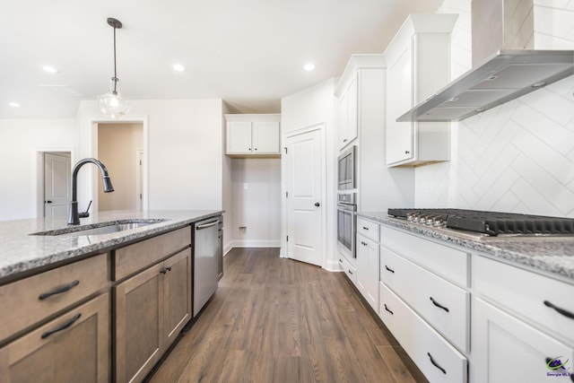 kitchen featuring stainless steel appliances, wall chimney range hood, white cabinets, light stone counters, and sink