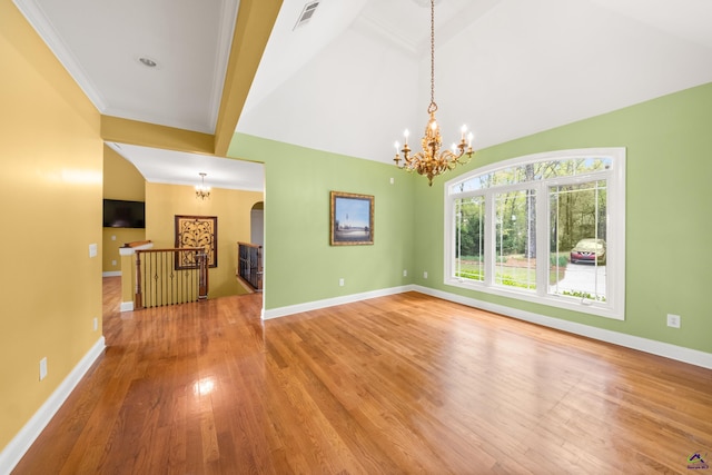 empty room featuring wood-type flooring, ornamental molding, a chandelier, and vaulted ceiling