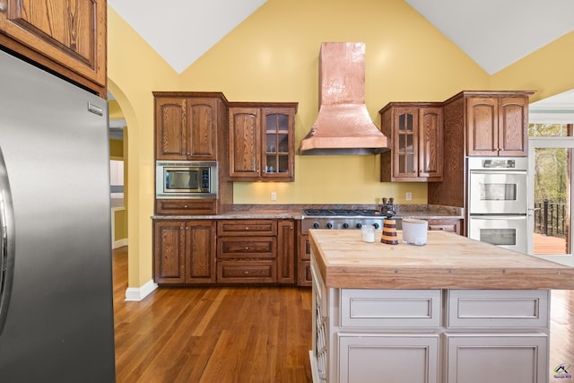 kitchen featuring a kitchen island, wood counters, premium range hood, appliances with stainless steel finishes, and dark wood-type flooring