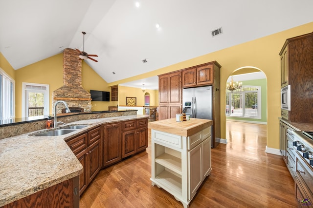 kitchen with wooden counters, a stone fireplace, a center island, sink, and ceiling fan