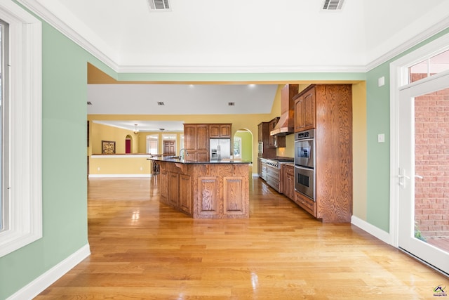 kitchen featuring crown molding, custom exhaust hood, light hardwood / wood-style floors, stainless steel appliances, and a center island with sink