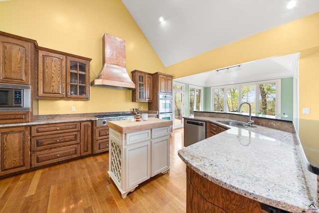 kitchen featuring a center island, sink, appliances with stainless steel finishes, custom range hood, and light hardwood / wood-style floors