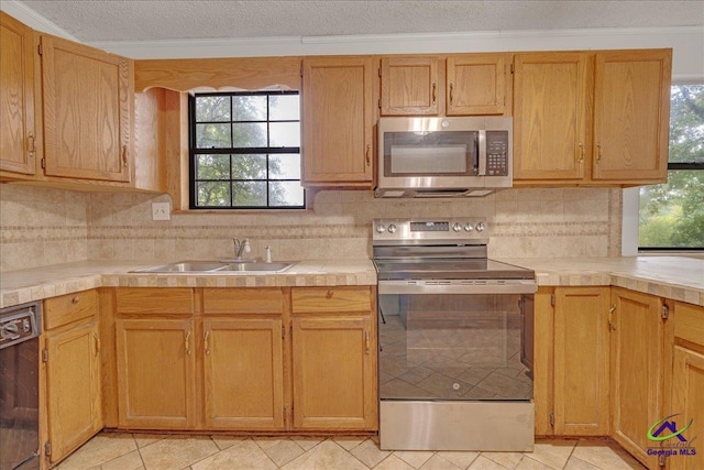 kitchen with crown molding, a textured ceiling, light tile patterned floors, stainless steel appliances, and sink