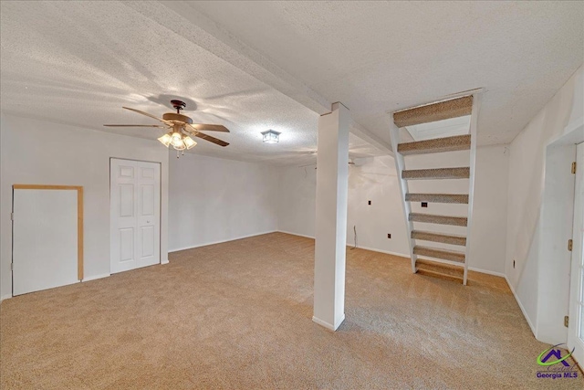 basement featuring a textured ceiling, light colored carpet, and ceiling fan