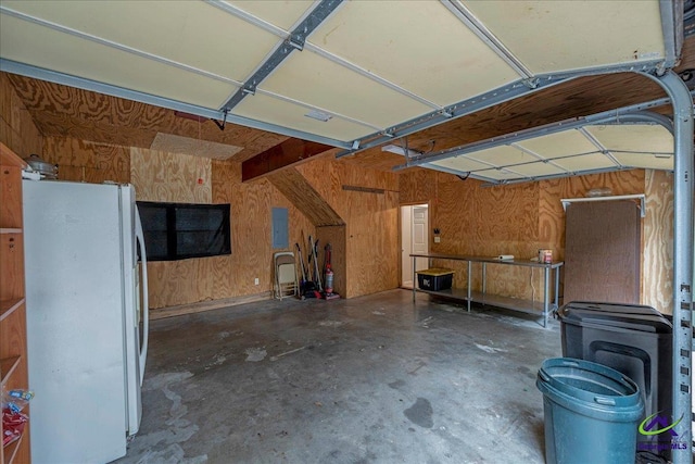 garage with white refrigerator, electric panel, and wood walls