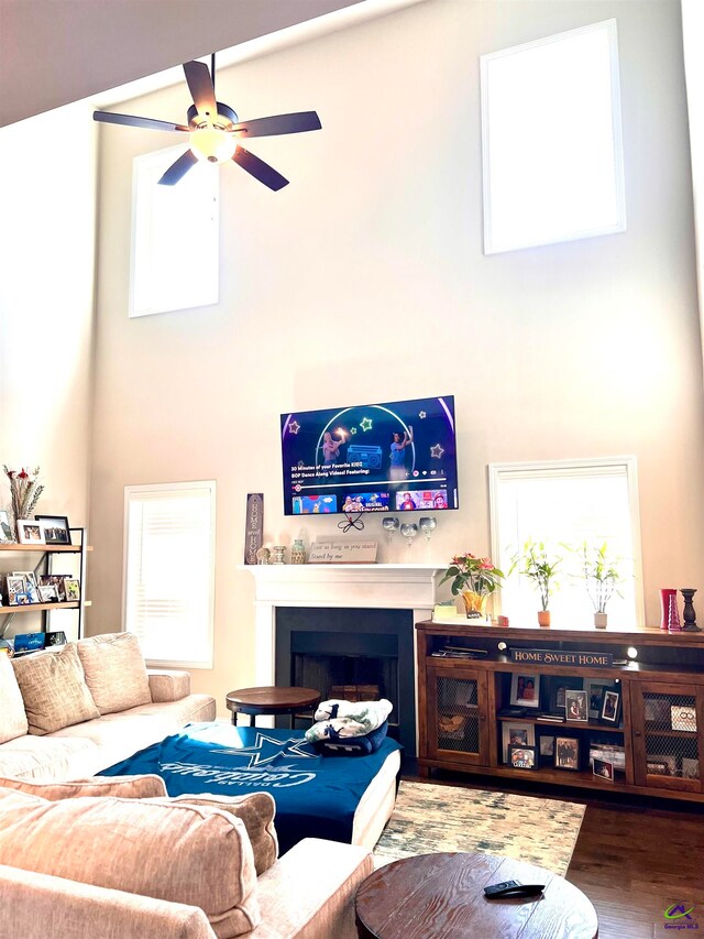 living room with ceiling fan, a high ceiling, and wood-type flooring