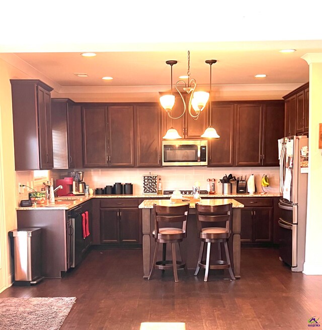 kitchen featuring dark brown cabinetry, decorative light fixtures, appliances with stainless steel finishes, a center island, and a kitchen bar