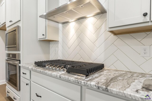 202 Bella Notte Cir, Warner Robins, GA 31088 - kitchen with white cabinets, stainless steel appliances, exhaust hood, backsplash, and light stone countertops