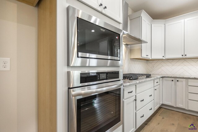 202 Bella Notte Cir, Warner Robins, GA 31088 - kitchen featuring wall chimney range hood, white cabinets, light wood-style flooring, backsplash, and appliances with stainless steel finishes