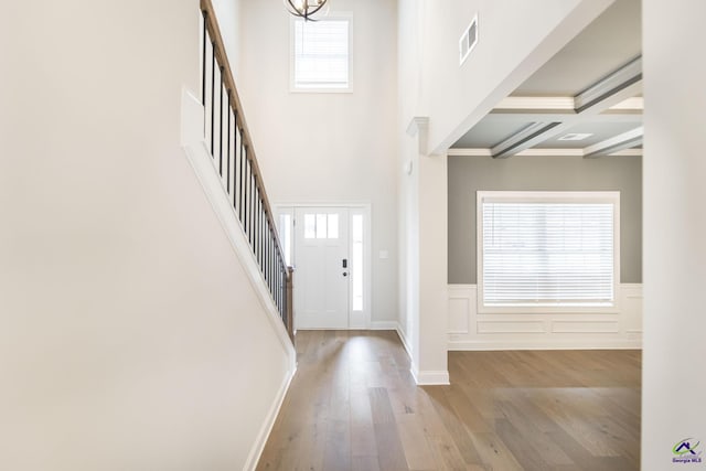 entryway featuring a high ceiling, coffered ceiling, a notable chandelier, light hardwood / wood-style floors, and beamed ceiling